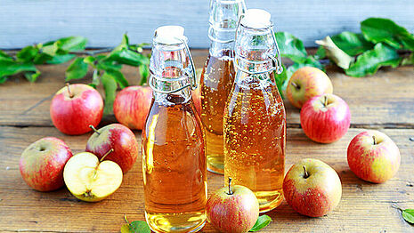 Three bottles with light brown liquid and apples
