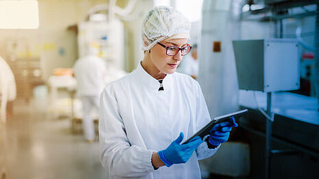 A woman in a hairnet and white robe is standing at the production site