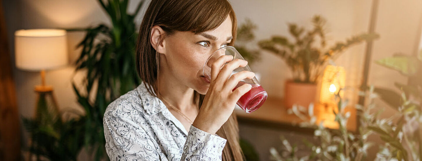 Frau trinkt an einem Glas mit einem roten Saft