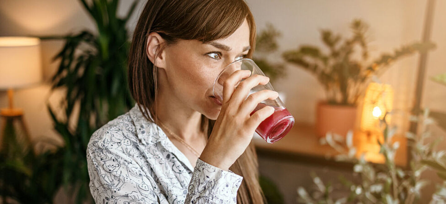 Frau trinkt an einem Glas mit einem roten Saft