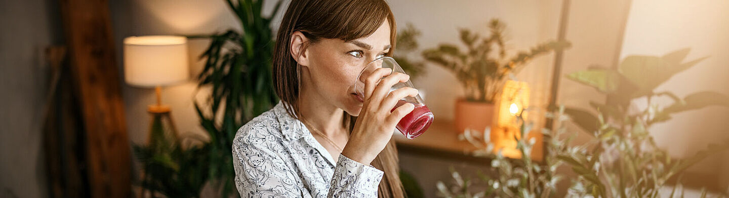 Frau trinkt an einem Glas mit einem roten Saft