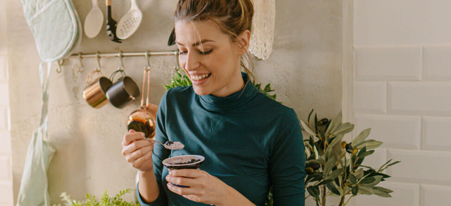 A woman eats yoghurt in the kitchen